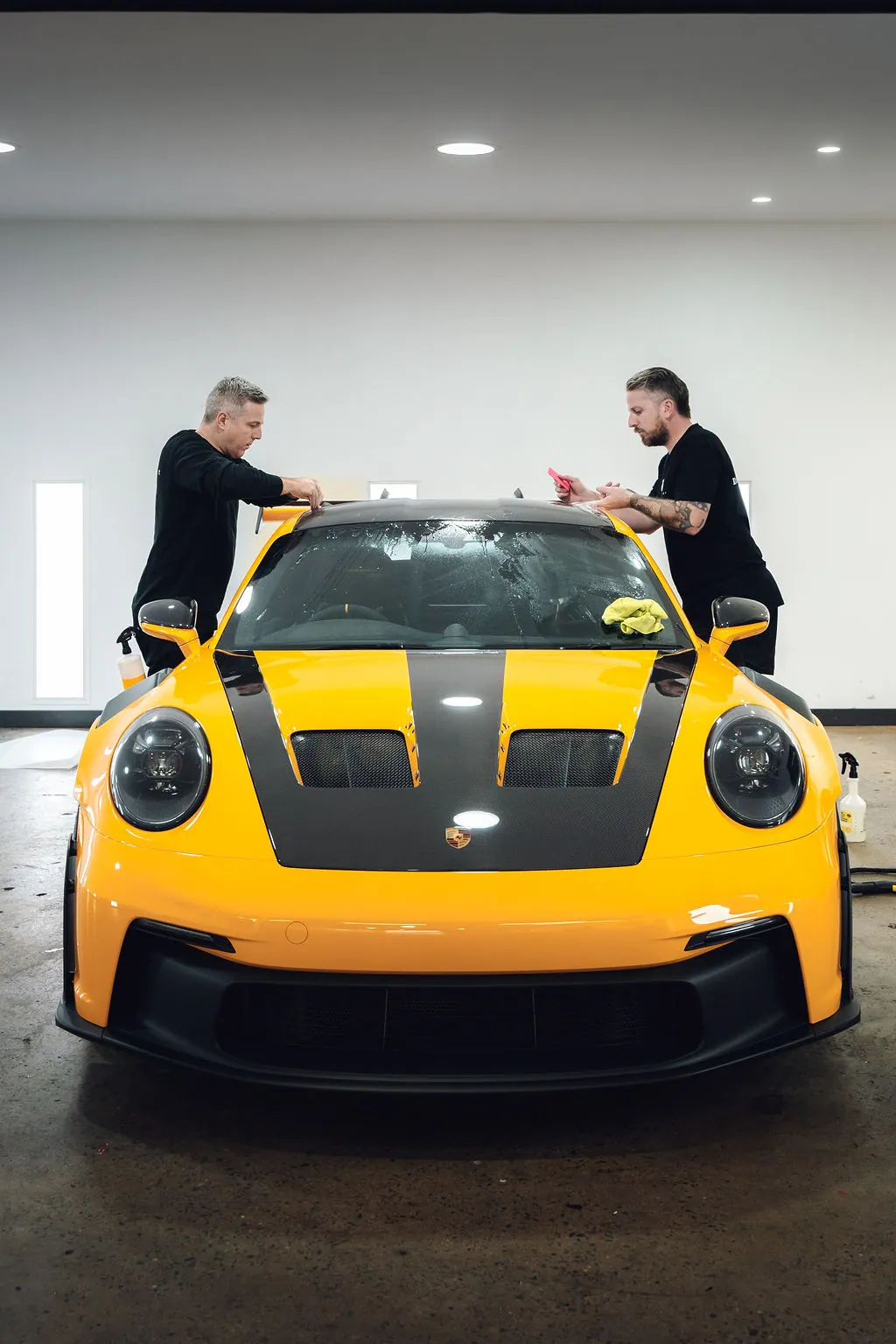 Two D&S installers fitting film to the front of a yellow GT3 RS