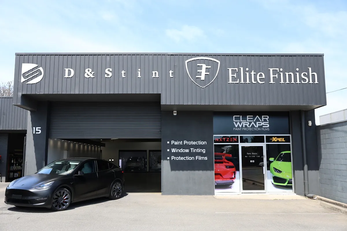 The D&S Tint studio at 15 Oaklands Rd: a black Tesla Model Y driving out of the roller door, and the Clear Wraps sign above the front door